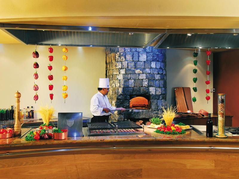 Chef preparing food in front of a wood-fired stone oven in a hotel restaurant.