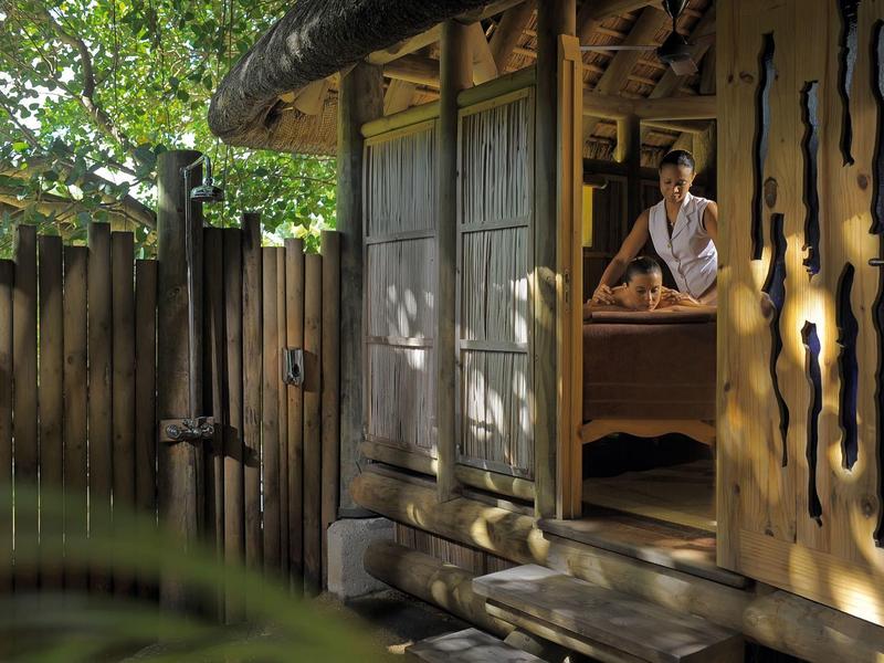 Man in white shirt sits on bed in rustic wooden cabin with garden