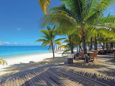 Palmy a dřevěná chodníková cesta podél bílé písečné pláže s čistým modrým mořem a oblohou.