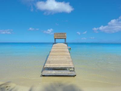 Holzsteg führt zu einem Stuhl über klarem, türkisfarbenem Meer unter blauem Himmel.