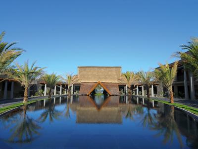 Complesso alberghiero moderno con grande piscina d'acqua e due file di palme e edifici.