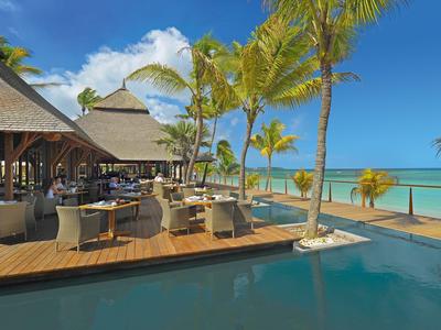 Otevřená restaurace s dřevěnou terasou, palmami a výhledem na tyrkysové moře pod modrou oblohou.