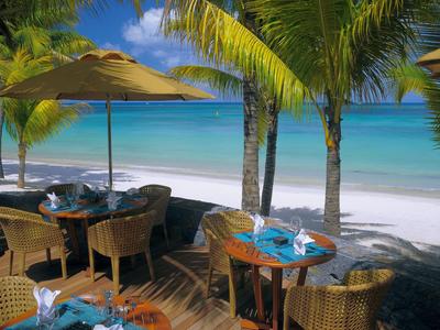 Strandrestaurant mit Tischen, Stühlen und Palmen am weißen Sandstrand und blauem Meer.