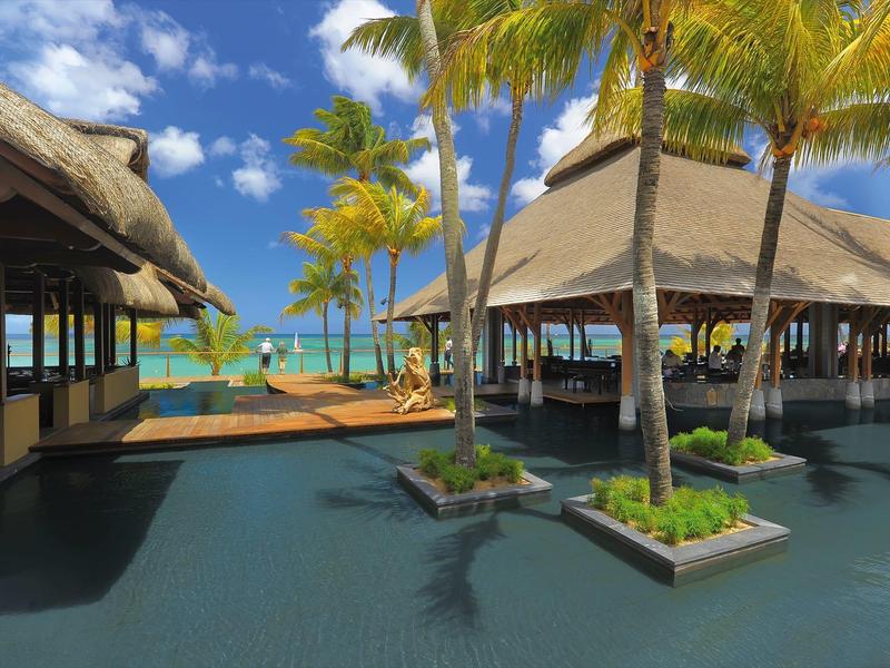 Luxusní resort s palmami, vodními prvky a výhledem na modré moře pod jasnou oblohou.