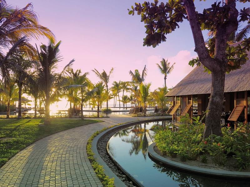 Křivá cesta vedle vody a stromů v tropickém resortu při západu slunce.