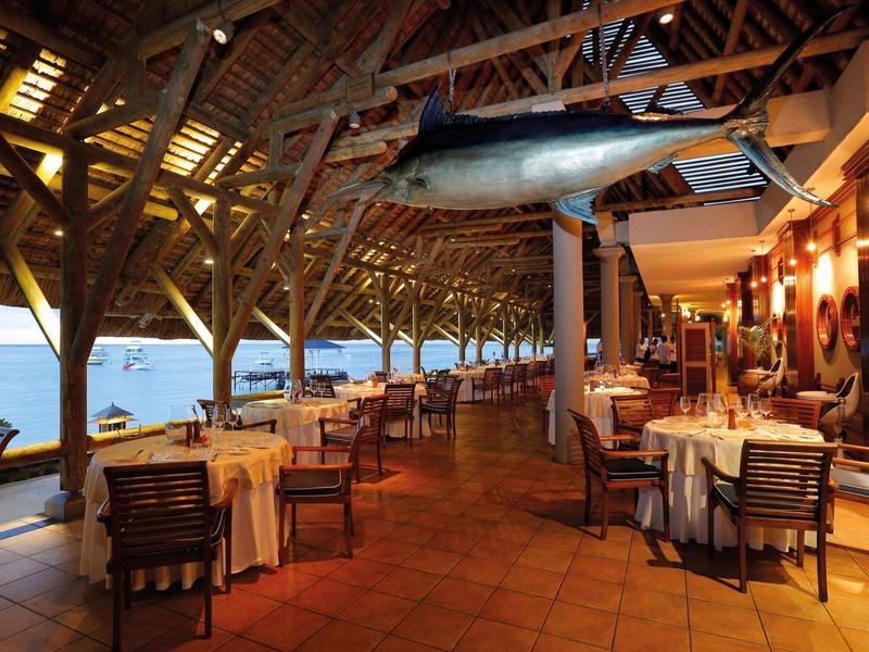 Offenes Restaurant mit Holzdach, Abendbeleuchtung und einem großen Fischmodell an der Decke.
