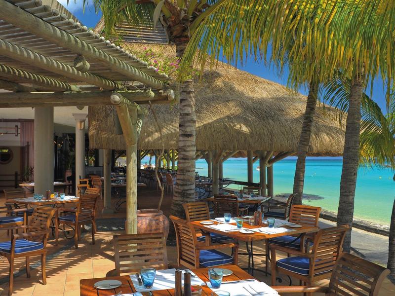 Strandrestaurant mit Holzmöbeln, Sonnenschirmen aus Palmblättern und Blick auf das türkisfarbene Meer.