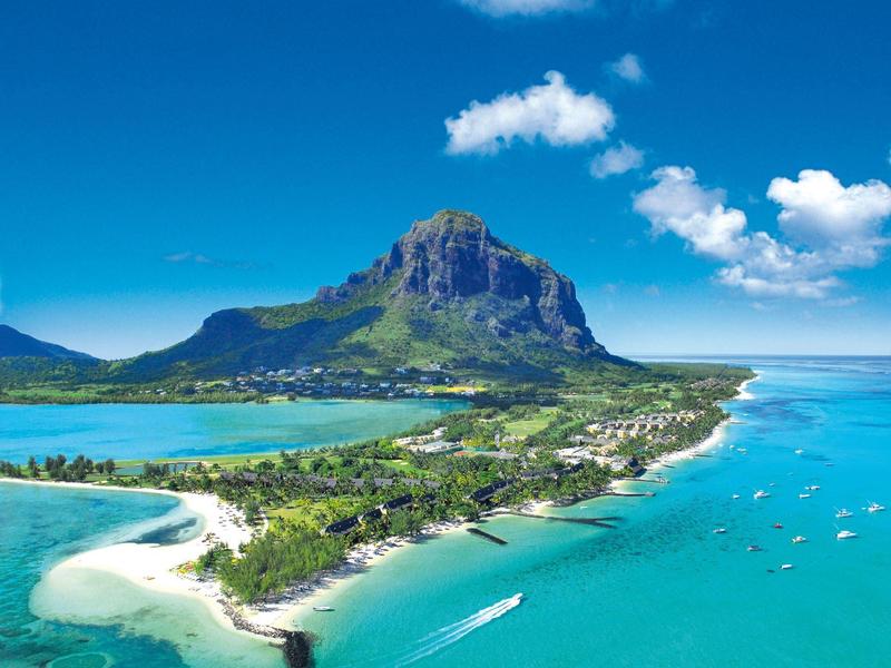 Tropische Küste mit klarem blauem Wasser, weißem Sandstrand und einem markanten Berg im Hintergrund.