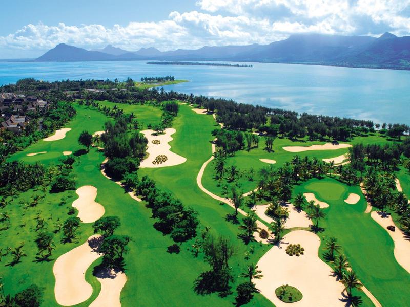 Grüner Golfplatz mit Sandbunkern und Küstenblick unter blauem Himmel bei Sonnenschein.