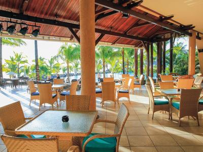 Offener Gastronomiebereich mit Holzdecke, Tischgruppen und durchgehender Sicht auf Palmen.