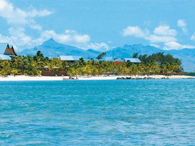 Klarer blauer Himmel über grün bewachsenem Küstenstreifen mit sandigem Strand und Bergen im Hintergrund.