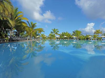 Großer blauer Pool mit Palmen und blauem Himmel sowie Wolken im Hintergrund.