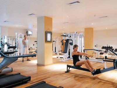 Moderner Fitnessraum mit Holzfußboden, verschiedenen Trainingsgeräten und zwei Personen beim Workout.