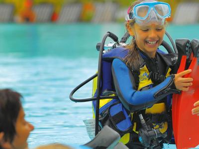 Kind in Tauchausrüstung lernt in einem Schwimmbecken mit einem Erwachsenen.