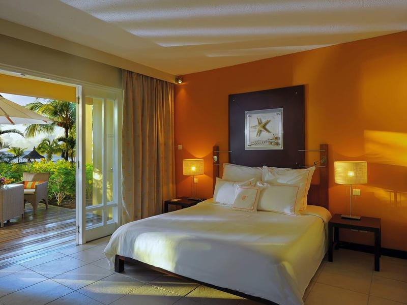 Modernes Schlafzimmer mit großem Bett, oranger Wand und Zugang zu einer Terrasse mit Pflanzen.