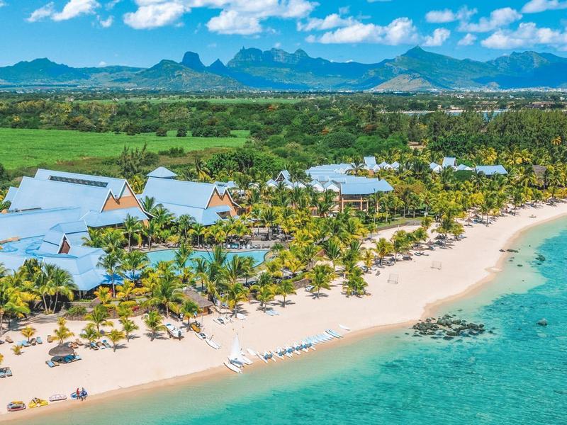 Strand mit weißem Sand, Palmen, blauer Lagune und grünen Hügeln im Hintergrund.