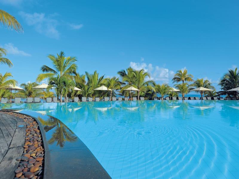 Großer blauer Pool mit Palmen und Sonnenschirmen unter klarem Himmel.