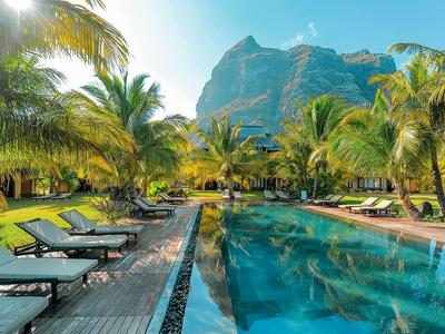 Bazén s lehátky obklopený palmami a horskou scenérií pod jasnou oblohou.