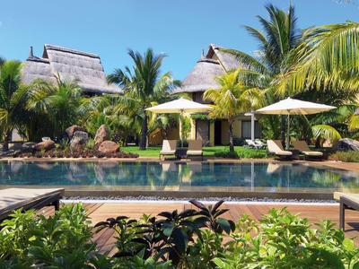 Luxusní bazénová oblast s deštníky, lehátky a tropickou zelení před budovami resortu.