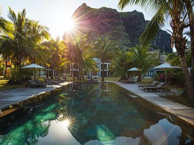 Poolbereich in tropischem Resort mit Palmen und Berg im Hintergrund bei Sonnenuntergang.