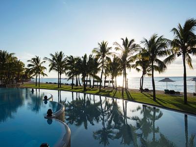Pool mit Palmen und Meerblick bei Sonnenuntergang in einem tropischen Resort.