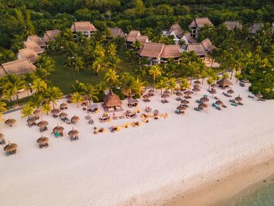 Vogelblick auf einen tropischen Strand mit Liegestühlen, Palmen und Resortgebäuden.