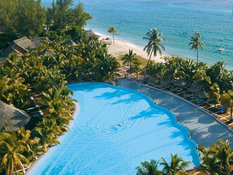 Výhled na bazén a pláž s palmami a modrou oblohou u moře.