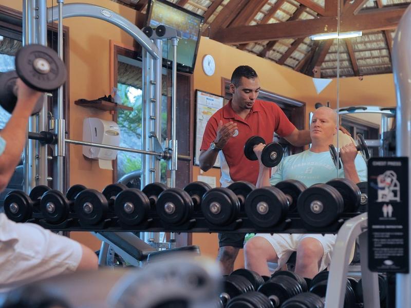 Dva muži cvičí s jednoručními činkami v moderní hotelové posilovně.