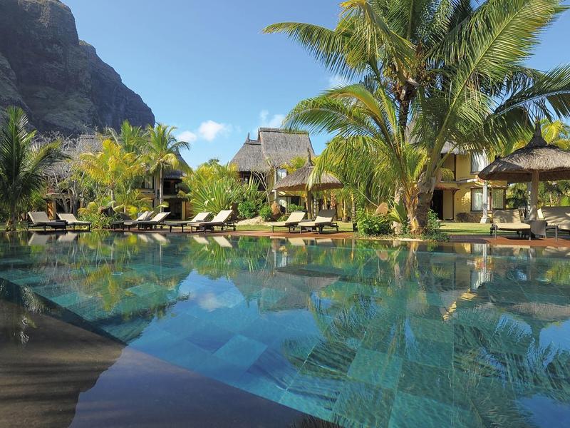 Luxusní bazénová oblast s palmami a lehátky před tropickými bungalovy