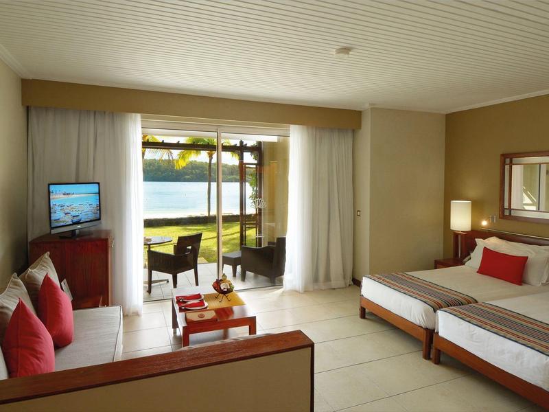 Helles Hotelzimmer mit Doppelbett, Sofa, Flachbild-TV und Balkon mit Seeblick und Tisch.