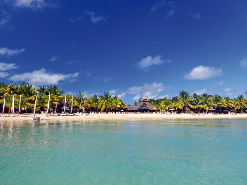 Klarer blauer Himmel über einem weißen Sandstrand mit Palmen und türkisblauem Wasser.