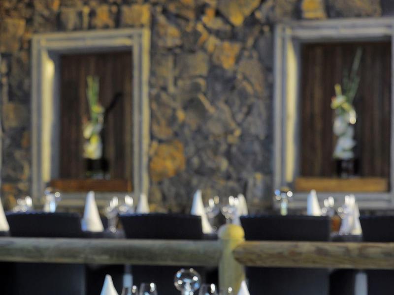 Restaurant mit steinverkleideten Wänden, schwarzen Tischen und weiß gefalteten Servietten.