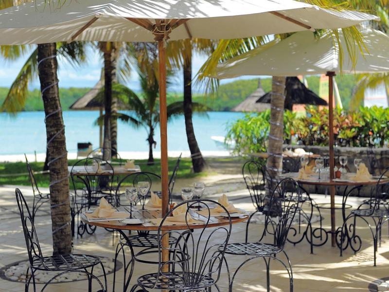 Freiluft-Café mit Eisenstühlen und Tischen unter weißen Sonnenschirmen am Strand nahe Palmen.