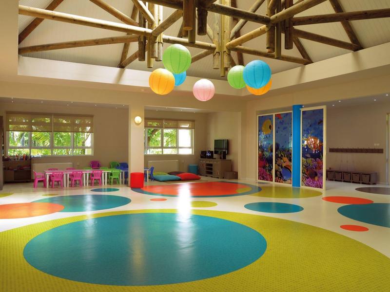 Heller Raum mit Holzdecke, großen bunten Punkten auf dem Boden und bunten Stühlen am Fenster.