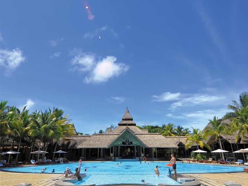 Großer Pool mit klarem Wasser, umgeben von Palmen, darunter Menschen und einen Pavillon am Ende.