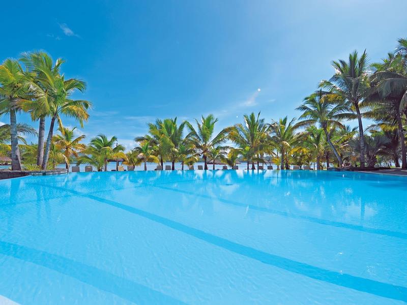 Großer Swimmingpool mit klarem Wasser, umgeben von Palmen und blauem Himmel.