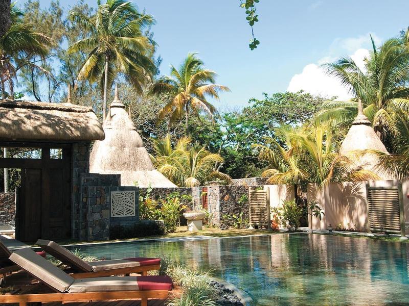 Tropischer Pool mit Liegestühlen, Palmen und klarem blauem Himmel an einem sonnigen Tag.