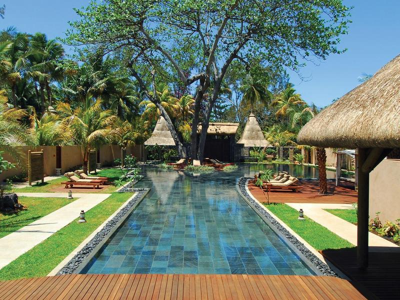 Ein langer Pool mit blau-grünen Fliesen, umgeben von grünen Bäumen und Strohdach-Hütten.