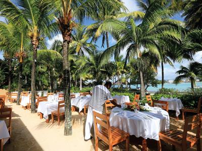Beachside restaurant with white tablecloths, wooden chairs, and palm trees in the background.