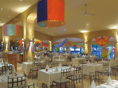 Bright restaurant with white-covered tables, colorful lamps, and warm-colored curtains.