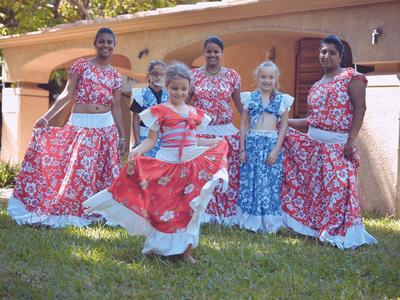 Fünf Frauen in bunten traditionellen Kleidern posieren im Garten vor einem Haus.