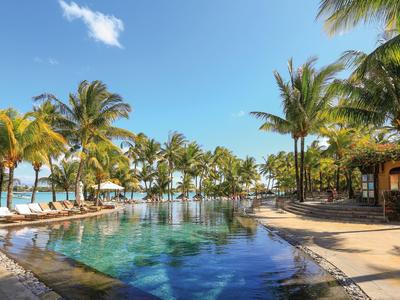 A tropical pool area with palm trees and lounge chairs under a clear sky.