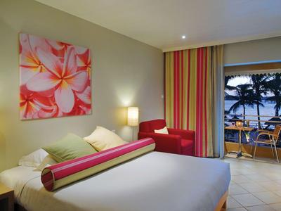 Hell eingerichtetes Hotelzimmer mit großem Bett und Blick auf eine Terrasse mit Meerblick.