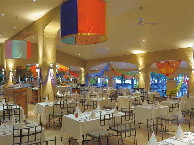 Bright restaurant with white-covered tables, colorful lamps, and warm-colored curtains.