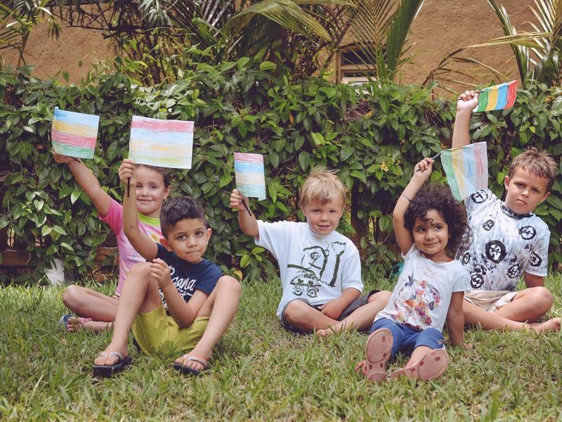 Five children sit on the grass holding small flags with colorful stripes.
