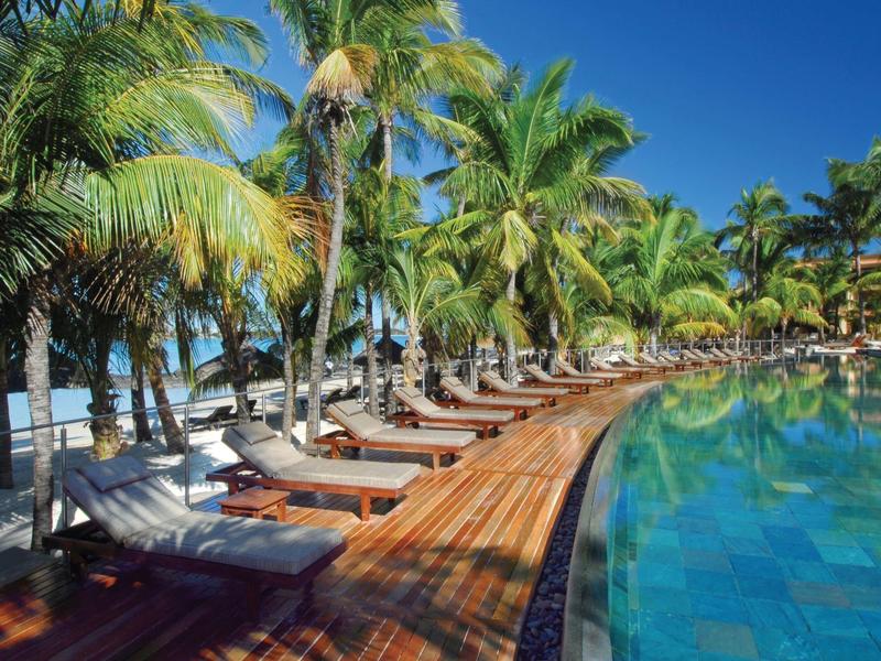Pool area with sun loungers and palm trees under clear blue sky