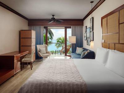 Geräumiges Hotelzimmer mit Bett, Sofa, Schreibtisch und Blick auf Balkon und Meer.
