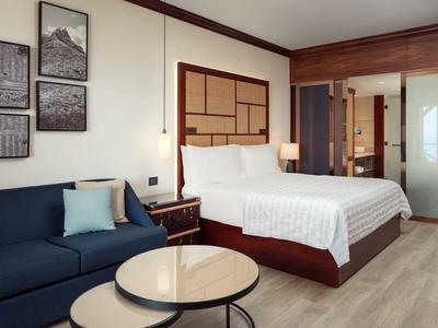 Moderne Hotelzimmer mit bequemem Doppelbett, Sofa, Nachttischen und hellem Holzboden.