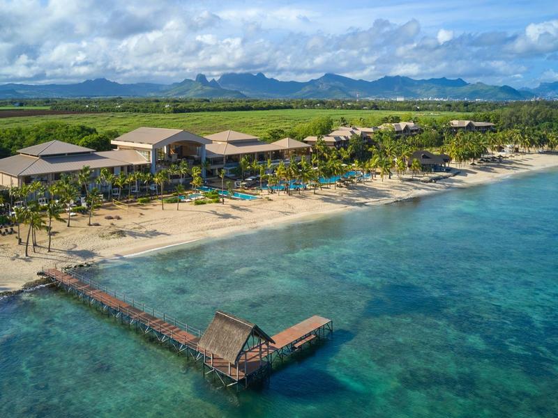 Strandresort met houten pier en helder water tegen bergachtergrond bij bewolkte lucht