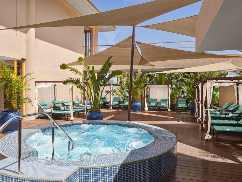 Bubbelbad met water, omgeven door ligbedden en zonneschermen op een hotelterras.